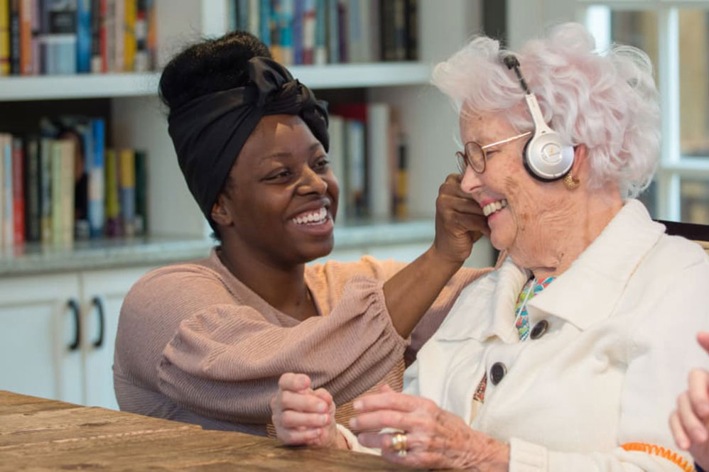 senior at Maplewood with headphones on talking with a caregiver
