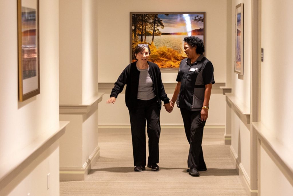 a senior woman holds hands with an employee while walking the halls